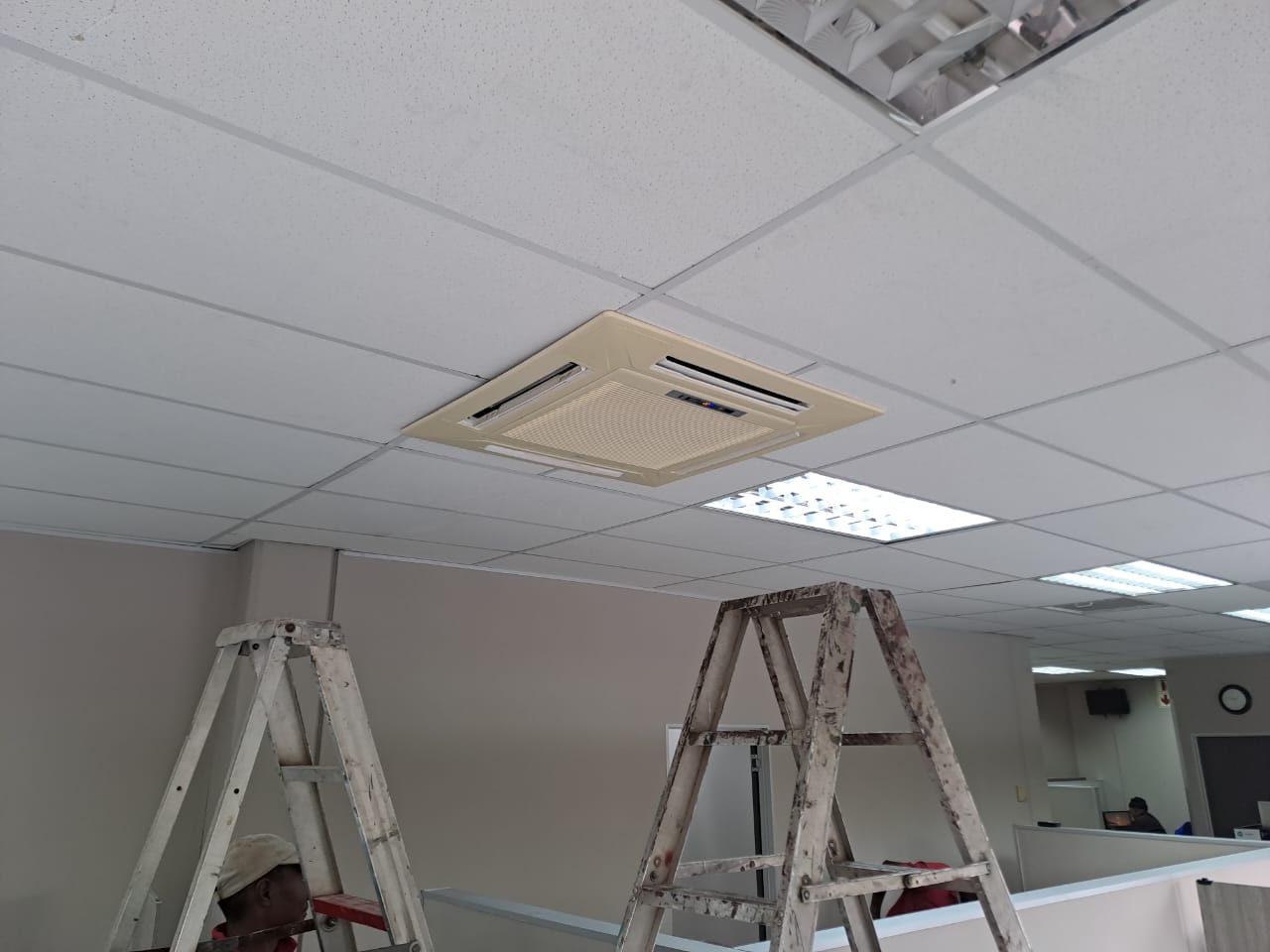 Technician installing commercial cassette air conditioner unit in office ceiling
