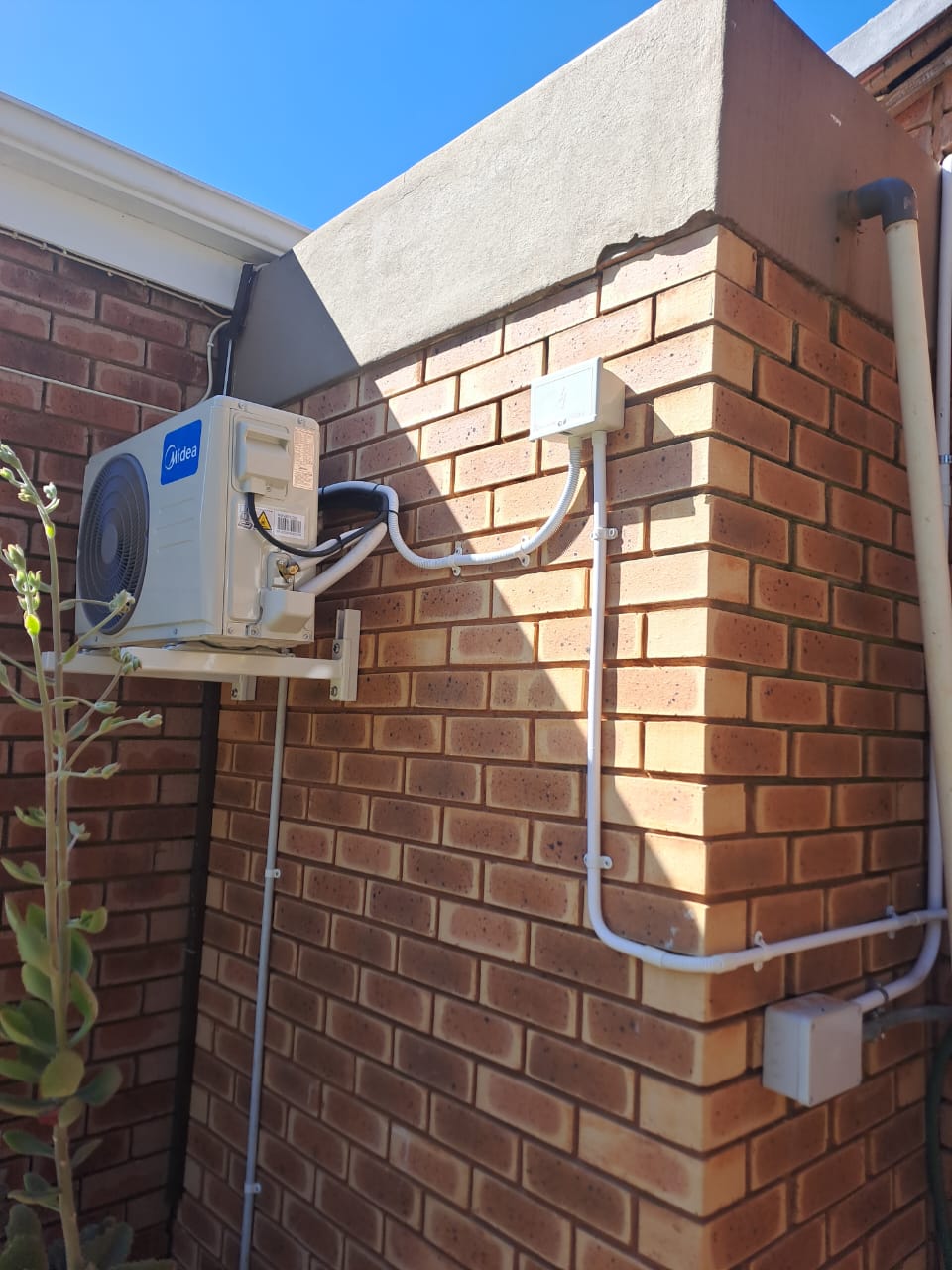 Midea outdoor air conditioner condenser unit mounted on brick wall with conduit piping